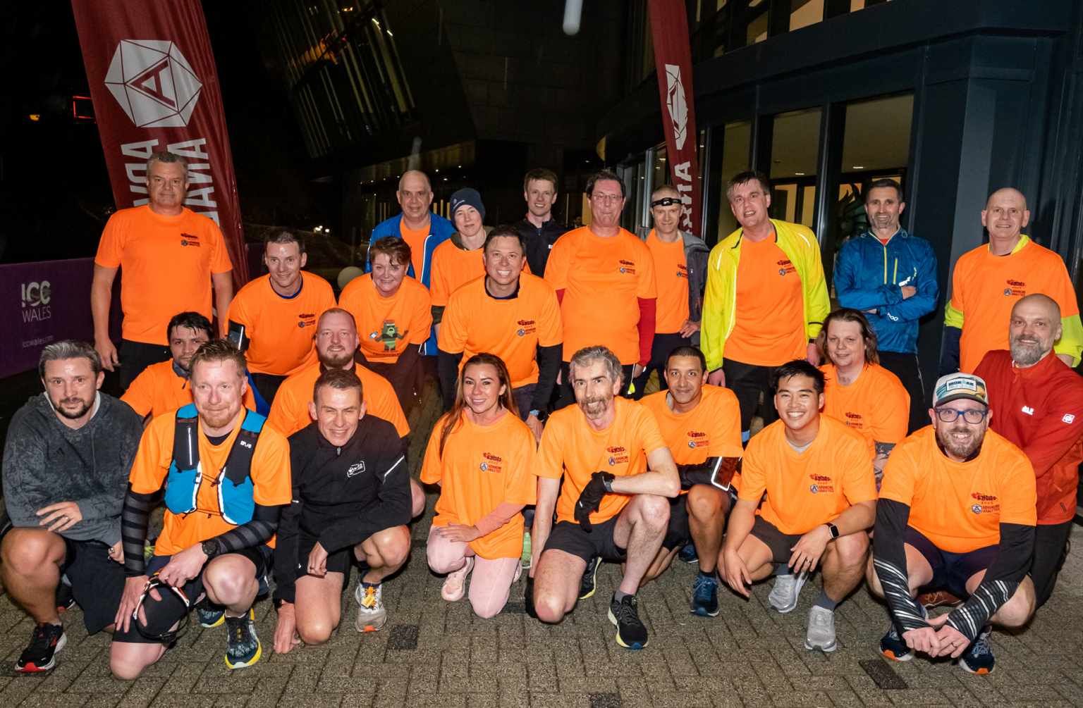 The image shows many runners after running the SQL Bits 5k, most are wearing an orange sqlbits running top, I am at the far left in a grey hoodie because I signed up late. It's dark and wet but everyone is still smiling.